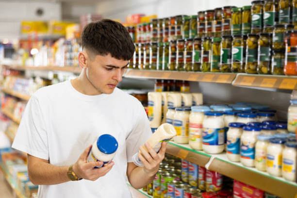 Hombre joven compara dos productos en supermercado leyendo la etiqueta. Los dueños de La Cosmopolitana cumplen con toda la normativa referente a etiquetado.