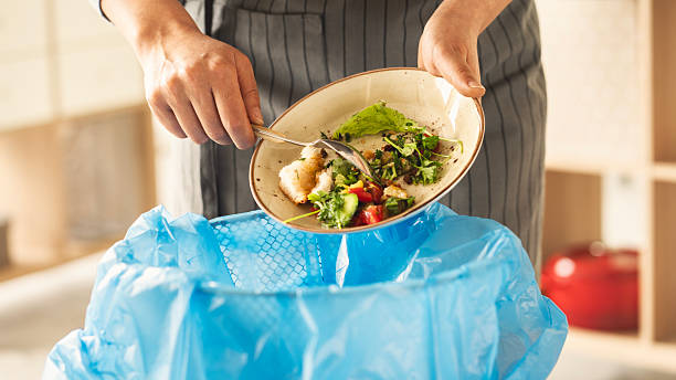 Close up a manos de persona tirando alimentos de un plato a un bote de basura. Los dueños de La Cosmopolitana impulsan medidas contra el desperdicio.