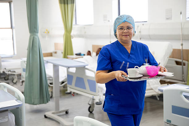 Trabajadora de la salud lleva bandeja con comida a paciente en camilla. La Cosmopolitana ofrece servicios de alimentación institucional.