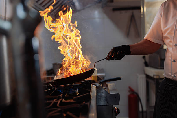 Close up a sartén con una llamarada en cocina industrial. La Cosmopolitana es consciente de los riesgos de calor en los servicios alimentarios.